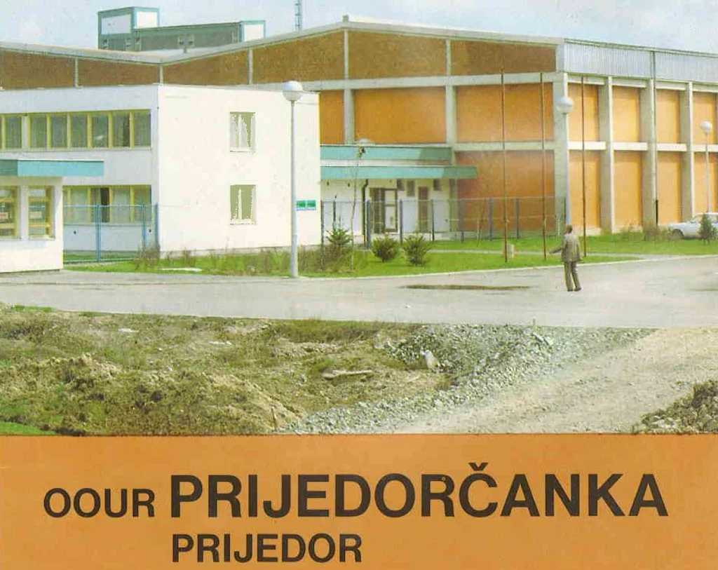 Zgrada stoji uz cestu; osamljen čovjek hoda po pločniku; u kontekstu industrijskog okruženja. Tekst: "OOUR PRIJEDORČANKA PRIJEDOR".